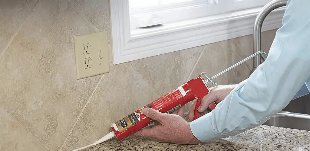 Handyman applying caulk along a kitchen backsplash and countertop seam in Boca Raton, FL